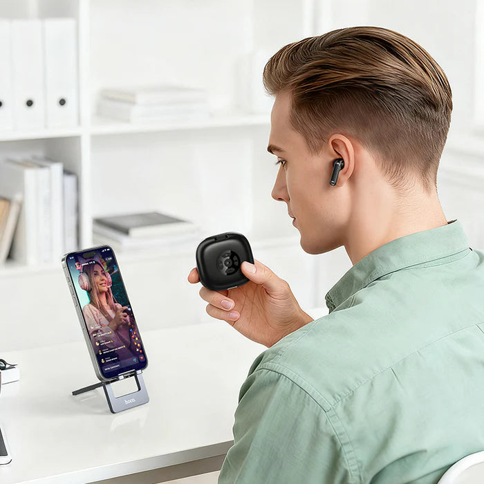 Person using HOCO wireless earbuds with a smartphone on a desk