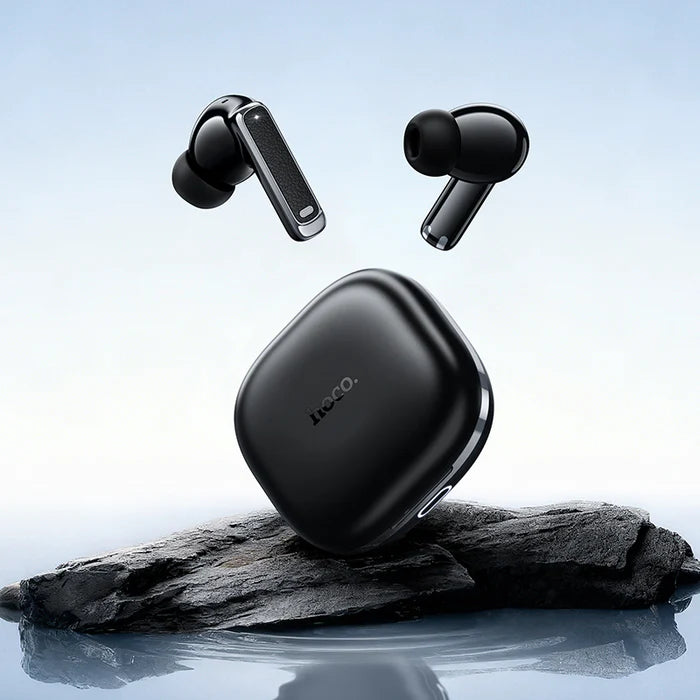 Black wireless earbuds with charging case on a rock by water