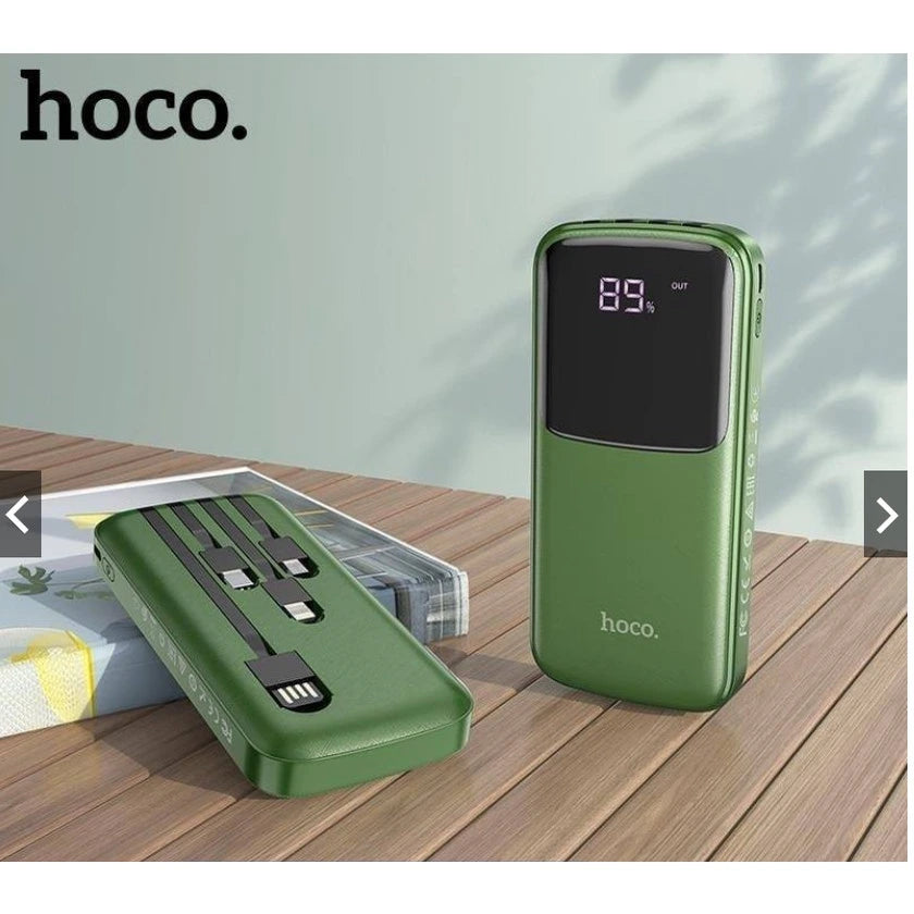 A lifestyle image of the green Hoco DB07 10000mAh power bank from LebTech Store Lebanon. One unit stands upright, showcasing its large LED digital battery percentage display, while another lies flat to reveal the four integrated charging cables (USB, Type-C, Lightning, and Micro-USB) neatly tucked into the back.
