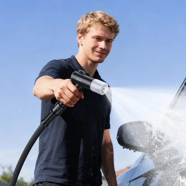 Man washing a car with a high-pressure washer against a clear blue sky.