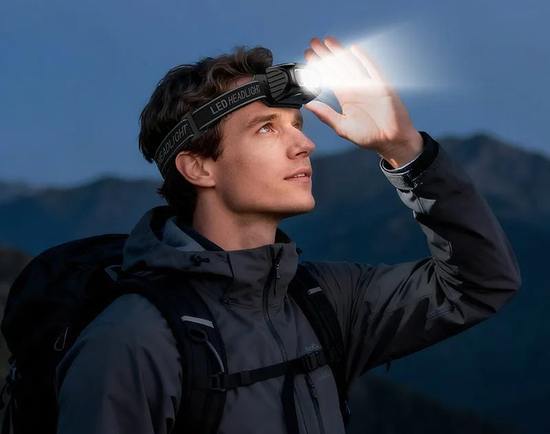 A hiker wearing the Hoco DL 24 rechargeable LED headlamp outdoors at night, demonstrating its bright beam, adjustable strap, and hands-free lighting utility available at Lebtech Store with fast delivery across Lebanon.