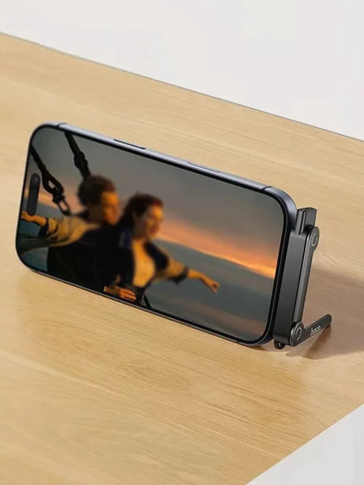  Hoco UA47 2-in-1 adapter plugged into an iPhone on a wooden desk, holding the phone horizontally in landscape mode as a sturdy desktop stand for watching movies, from Lebtech Store Lebanon.
